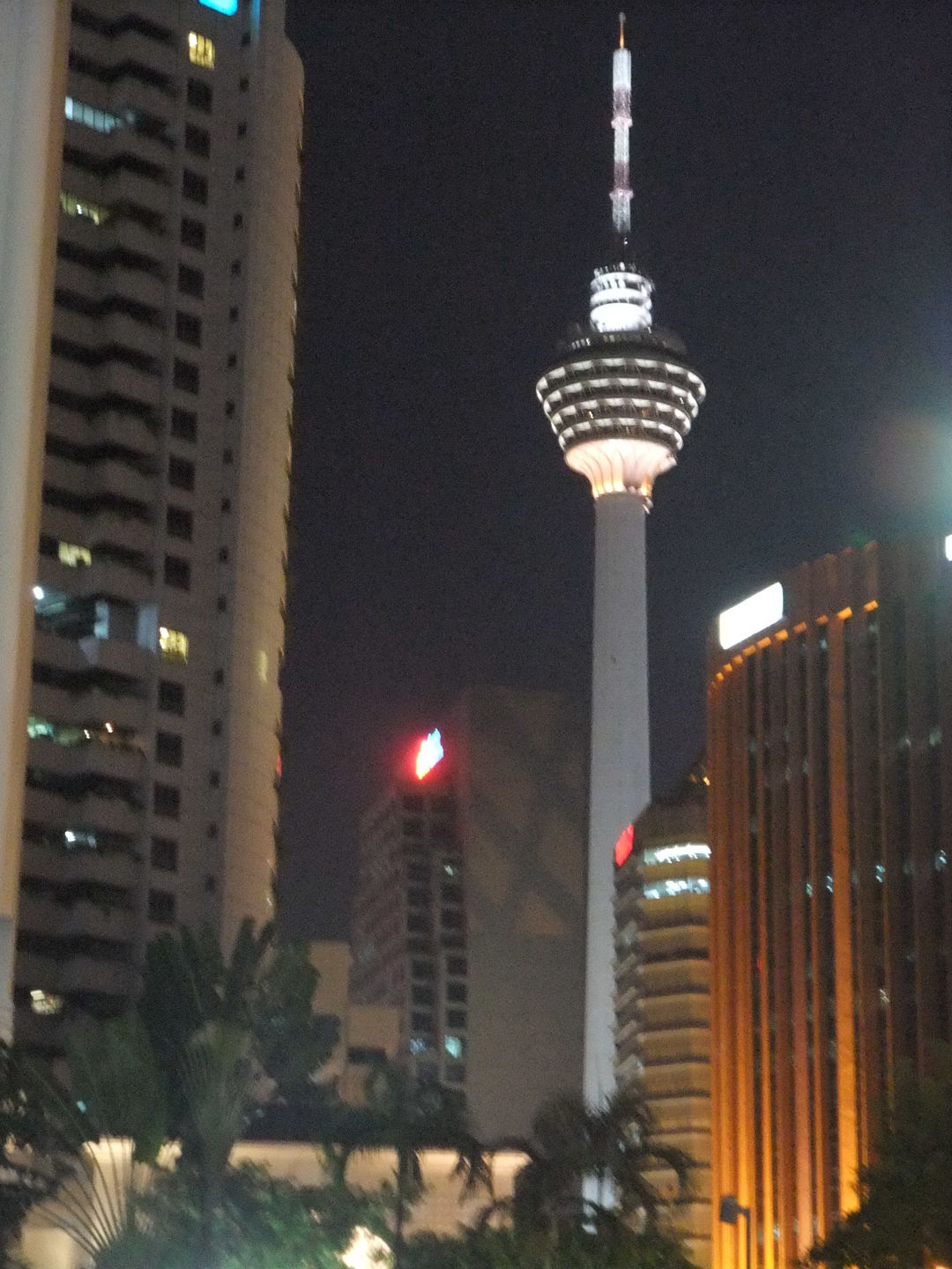 KL Tower illuminated at night with city lights and surrounding skyscrapers